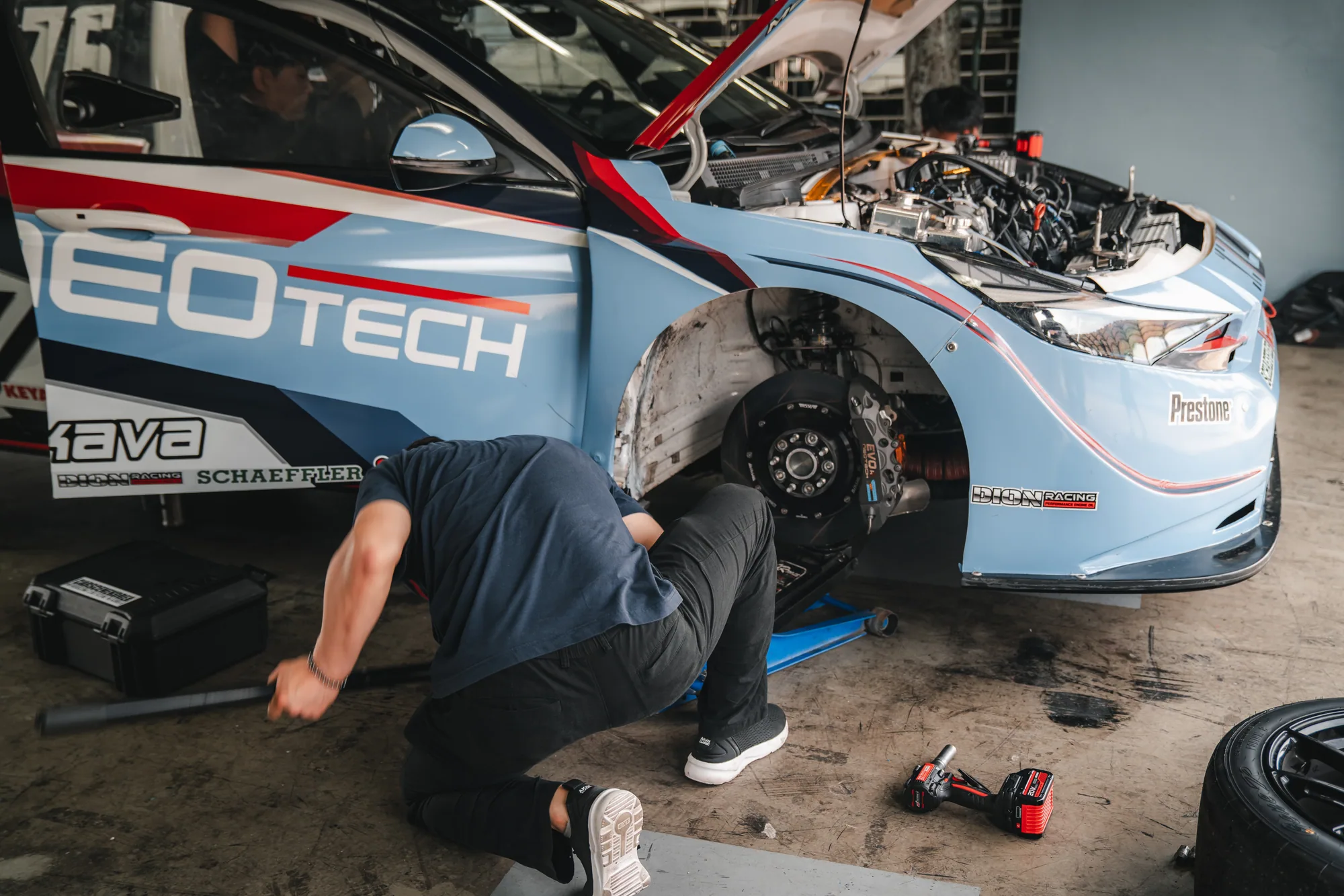 Mechanic jacking a NEOTECH-liveried race car with the front wheel off in the pit